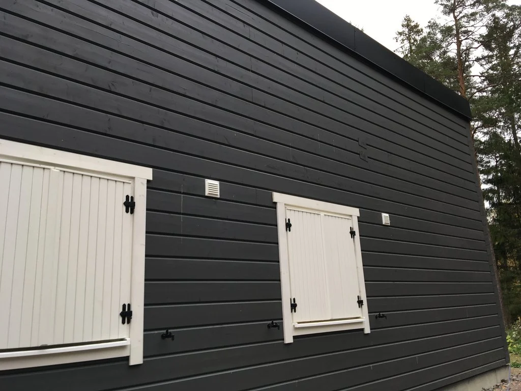 Galler till friskluftsventiler bredvid fönster på en mörk träfasad, villa i Gnesta kommun